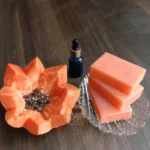 Papaya Soap Bars And Papaya With A Dropper Bottle On A Wooden Surface, Labelled &Quot;Dm Traders Organic Store.&Quot;