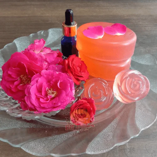 A Glass Plate With Roses, A Small Bottle, And Two Bars Of Rose Soap From Dm Traders Organic Store.